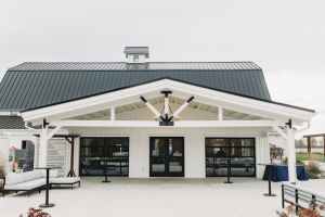 Front view of a modern building with a black metal roof, white walls, and large glass doors under a covered porch.